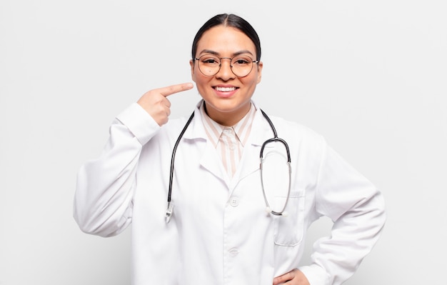 Mujer hispana sonriendo con confianza apuntando a su propia sonrisa amplia, actitud positiva, relajada y satisfecha