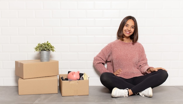 Mujer hispana sonriendo felizmente con una mano en la cadera y actitud confiada, positiva, orgullosa y amistosa