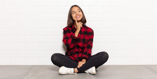 Mujer hispana sonriendo felizmente y soñando despierto o dudando, mirando hacia el lado