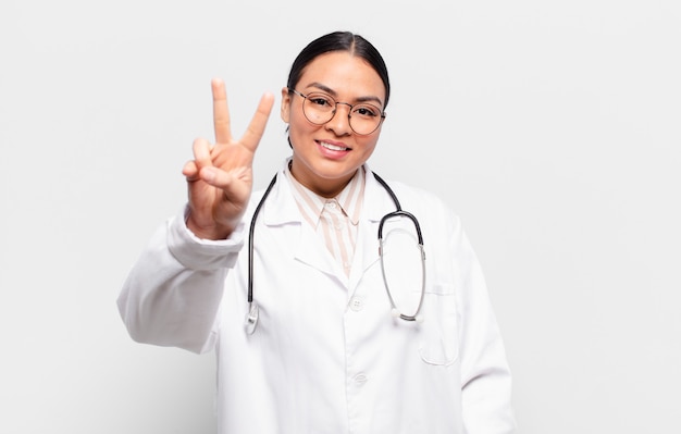 Mujer hispana sonriendo y luciendo feliz, despreocupada y positiva, gesticulando victoria o paz con una mano