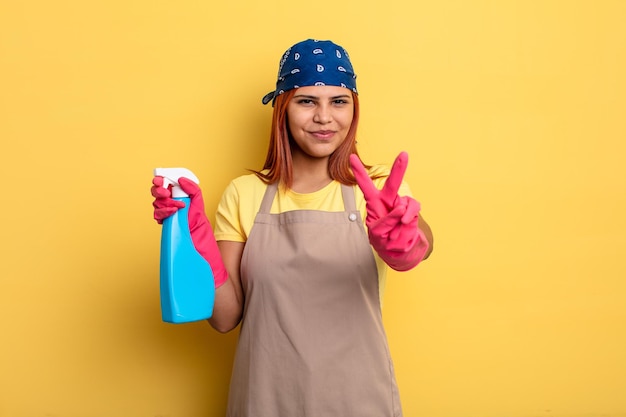 Mujer hispana sonriendo y luciendo feliz, gestando victoria o paz. concepto de limpieza y ama de llaves