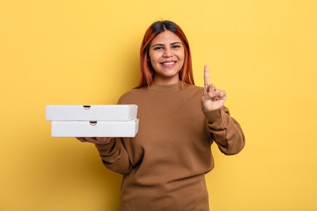 Mujer hispana sonriendo con orgullo y confianza haciendo el número uno. concepto de pizzas para llevar