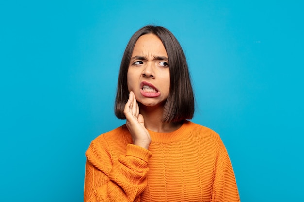 Mujer hispana sosteniendo la mejilla y sufriendo dolor de muelas, sintiéndose enferma, miserable e infeliz, buscando un dentista