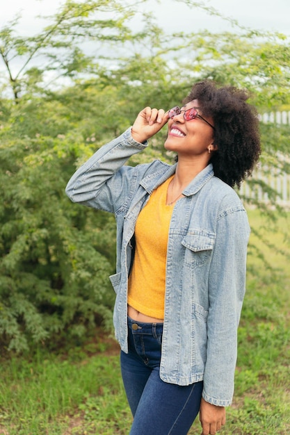 Mujer hispana sosteniendo sus gafas de sol mientras posa con plantas verdes en el fondo