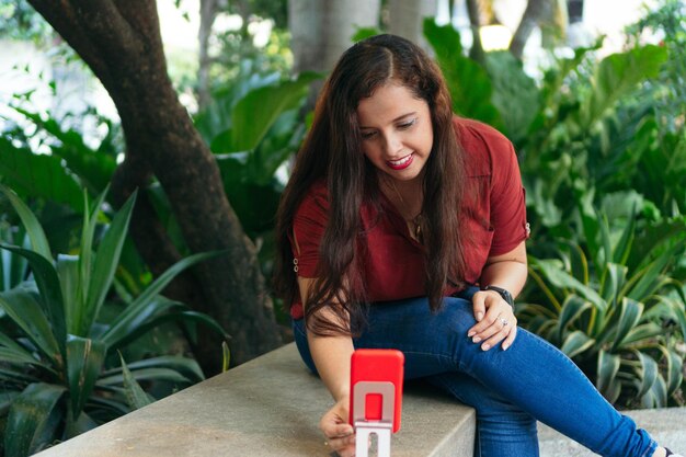 Mujer hispana tomando fotos con la cámara del teléfono móvil en el parque