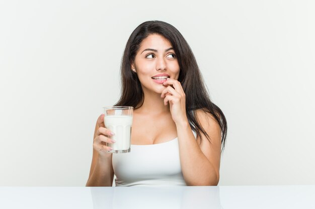 La mujer hispánica joven que sostenía un vaso de leche se relajó pensando en algo que miraba un espacio de la copia.