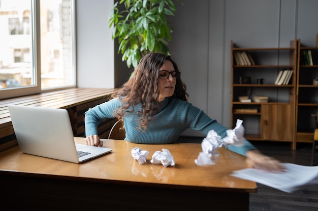 Una mujer histérica que tira documentos en papel arrugado sufre de agotamiento y exceso de trabajo