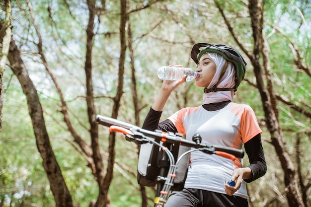 Mujer con hiyab bebiendo una botella de agua mineral cuando tiene sed