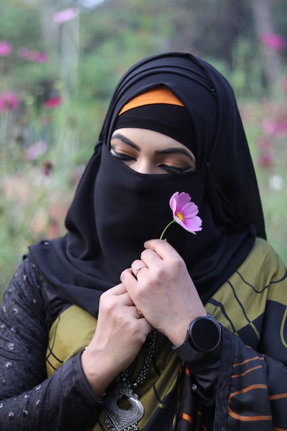 Una mujer con un hiyab negro sostiene una flor en sus manos.