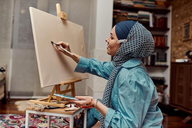 Una mujer con hiyab pinta sobre lienzo con pincel y témpera
