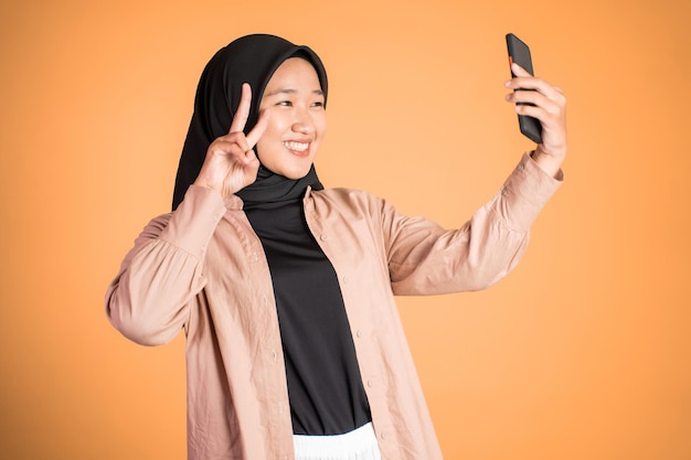 Mujer en hiyab sosteniendo un teléfono inteligente para selfie