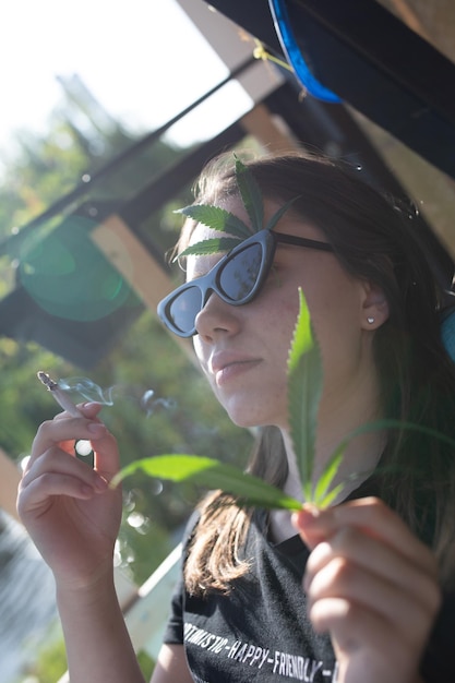 Foto mujer con hojas de cannabis mientras fuma un cigarrillo
