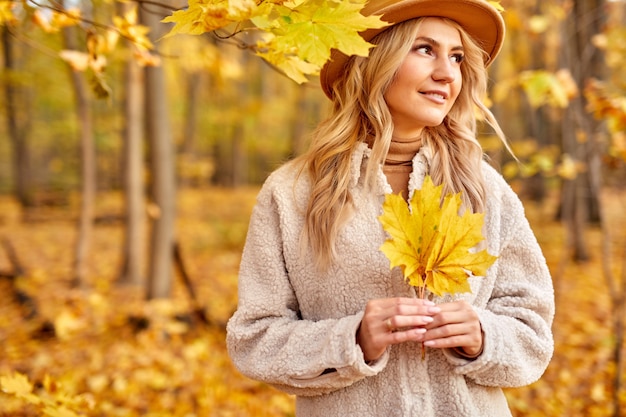 Mujer con hojas de otoño en la naturaleza soleada, parque o bosque. dama con sombrero camina