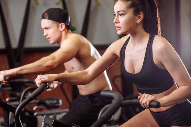 Mujer y hombre en bicicleta en el gimnasio, ejercitar las piernas haciendo bicicletas de ciclismo de entrenamiento cardiovascular