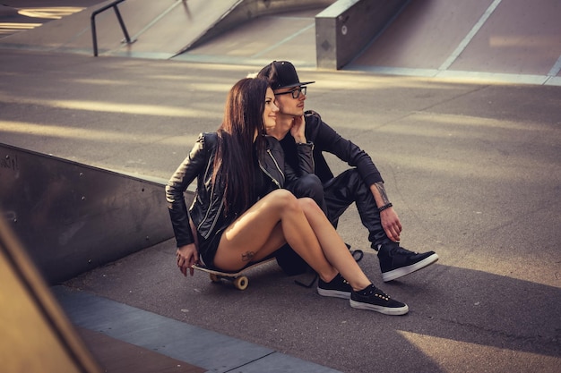 Mujer y hombre casuales se sientan en patineta en un parque de patinaje.