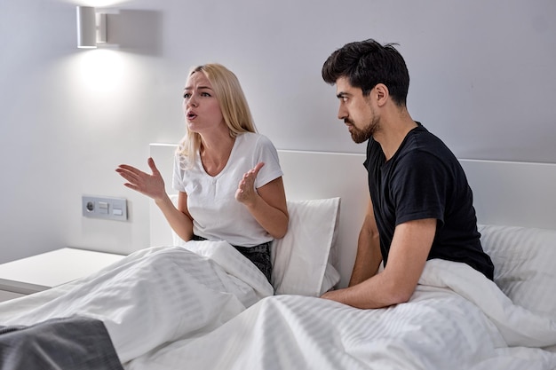 Mujer y hombre caucásicos furiosos durante una discusión en casa, sentados juntos en la cama