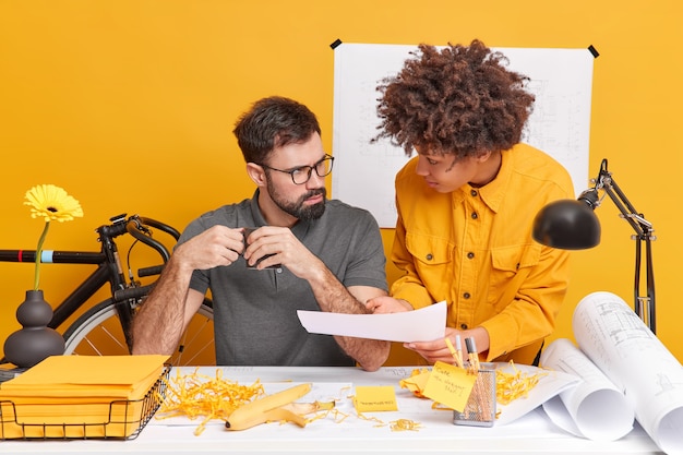 La mujer y el hombre concentrados colaboran en la pose de información en el escritorio durante el tiempo de trabajo en la oficina moderna discutir el proyecto arquitectónico rodeado de planos