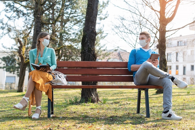 Mujer y hombre en distanciamiento social sentado en un banco