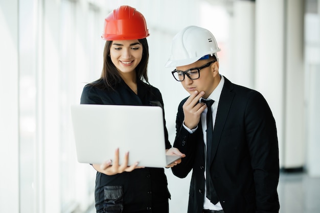 Mujer y hombre empresario y arquitecto en hemlet en reunión de negocios, mirando la computadora portátil en planes de construcción