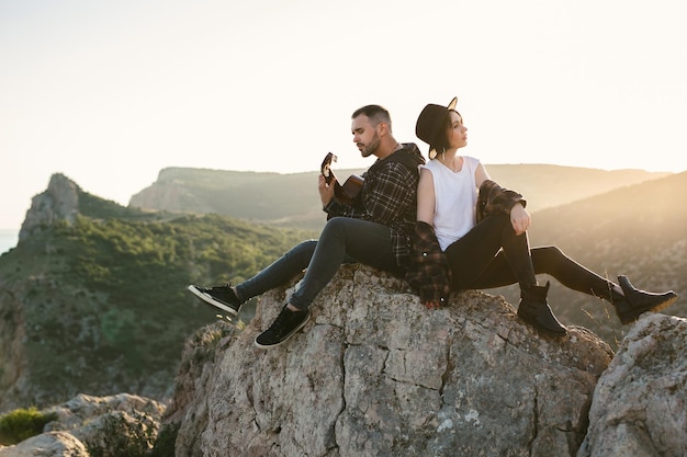 Una mujer y un hombre con una guitarra están sentados en una roca con vistas al mar.