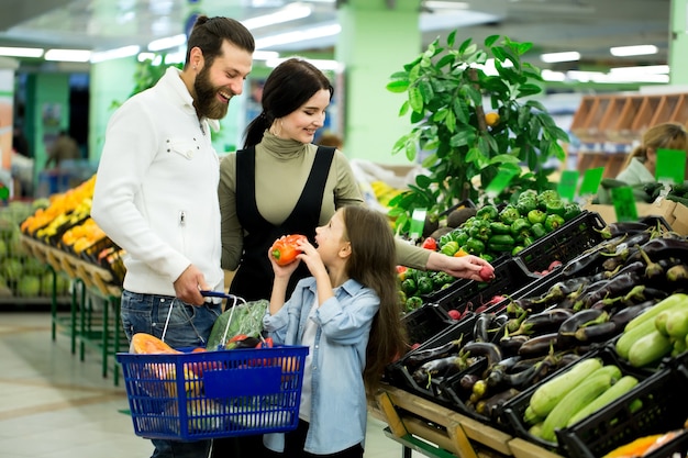 Una mujer con un hombre y un niño, eligiendo verduras mientras compra en un supermercado de verduras