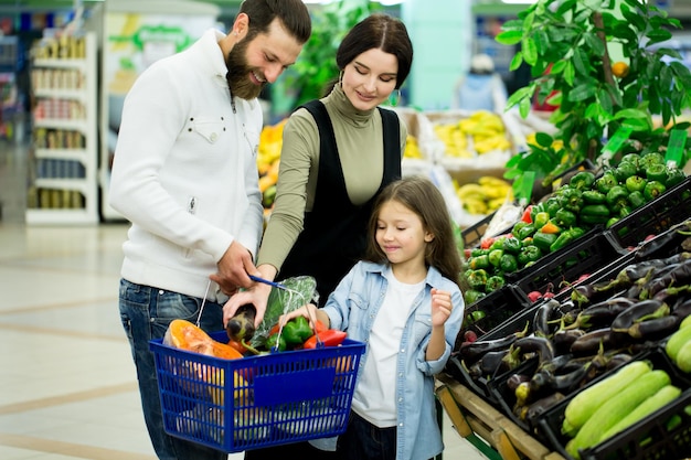 Una mujer con un hombre y un niño eligiendo verduras mientras compran en un supermercado de verduras