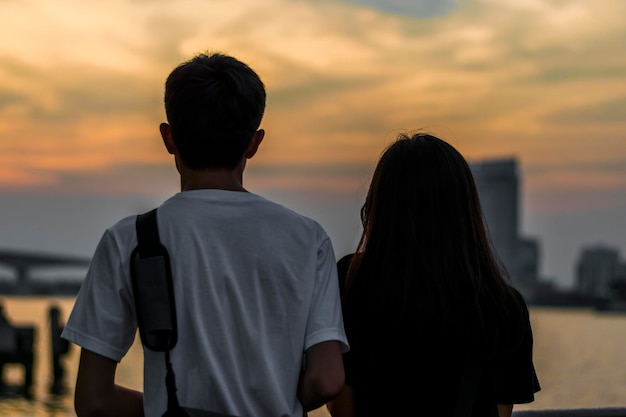 Mujer con hombre de pie junto al agua, con vistas a la ciudad y al puente