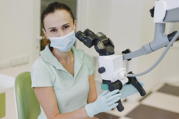 Una mujer en un hospital con mascarilla y guantes sostiene un microscopio.