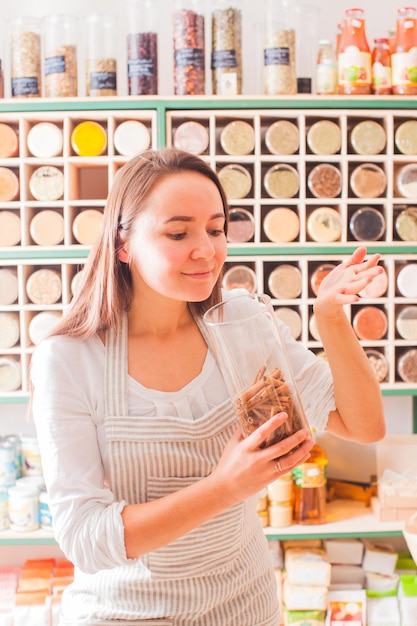 La mujer huele el aroma de la canela en el tarro de cristal. Especias frescas en la cocina del chef.