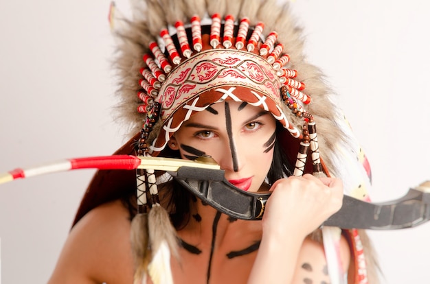 Foto la mujer en la imagen de los pueblos indígenas de américa con un arco y una flecha posa sentada sobre un fondo claro