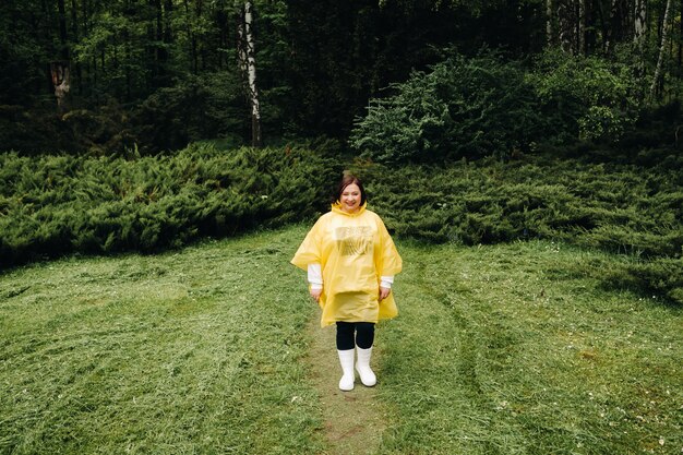 Una mujer con un impermeable amarillo camina en el parque en el verano después de la lluvia.