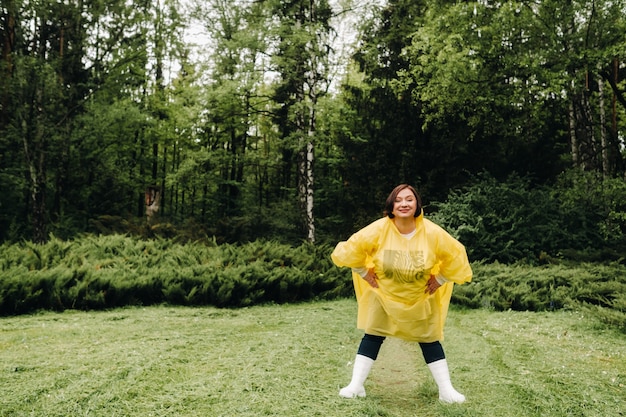 Una mujer con un impermeable amarillo muestra emociones en el parque en el verano después de la lluvia