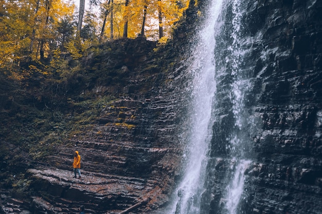 Mujer en impermeable amarillo en otoño concepto de senderismo cascada