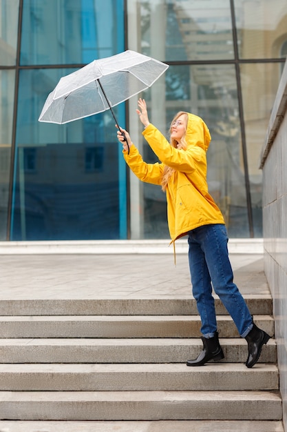 Mujer de impermeable amarillo con paraguas en la ciudad