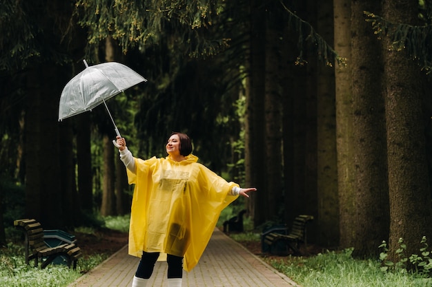 Una mujer con un impermeable amarillo y una sombrilla camina en el parque y el jardín en verano.