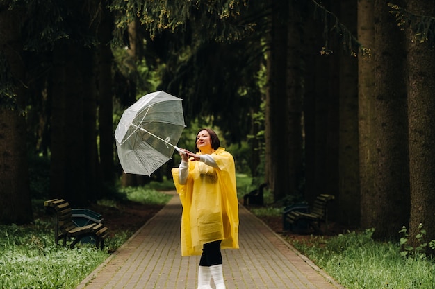 Una mujer con un impermeable amarillo y una sombrilla camina en el parque y el jardín en verano.