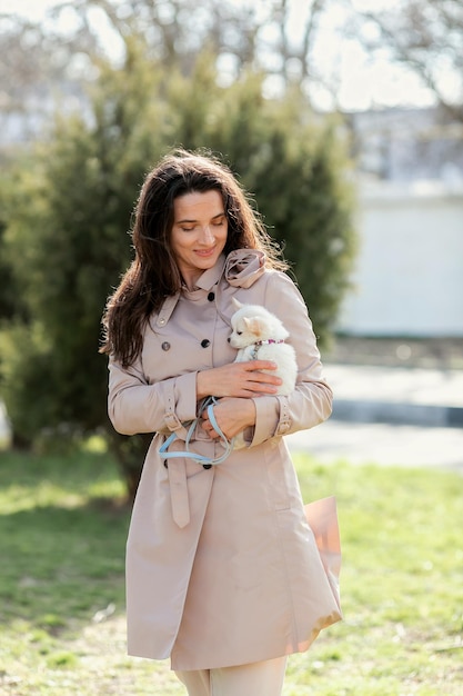 una mujer con un impermeable ligero camina y juega con un pequeño perro blanco