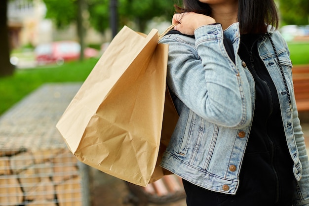 Mujer de incógnito sosteniendo varias bolsas de papel con cosas compradas caminando al aire libre en el parque, chica después de ir de compras.