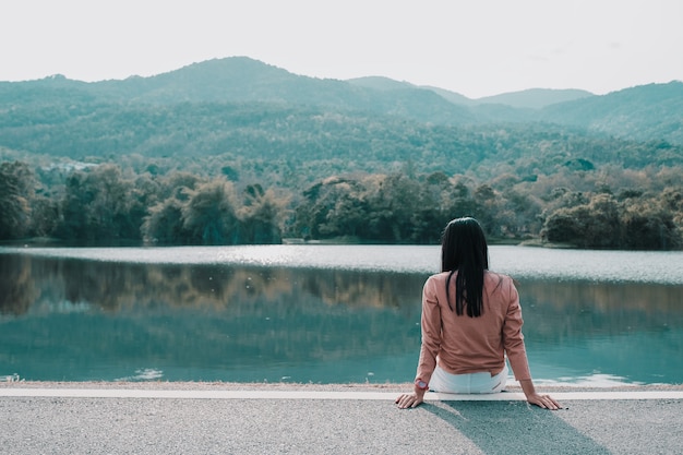 Mujer inconformista que se sienta solamente en el parque en fondo del moutain con el espacio de la copia.