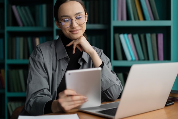 Mujer independiente con anteojos que trabaja en el espacio de coworking de la oficina usa una computadora portátil hace un informe de la empresa