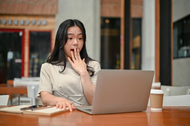 Una mujer independiente asiática asombrada miró la pantalla de su computadora portátil con una cara sorprendente