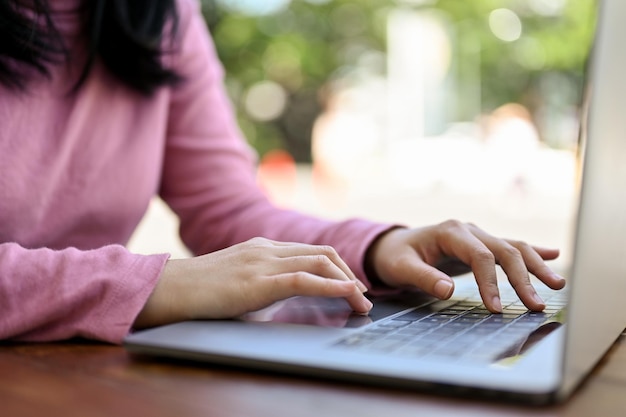 Mujer independiente asiática que trabaja a distancia en el café usando una computadora portátil sentada afuera o en el café