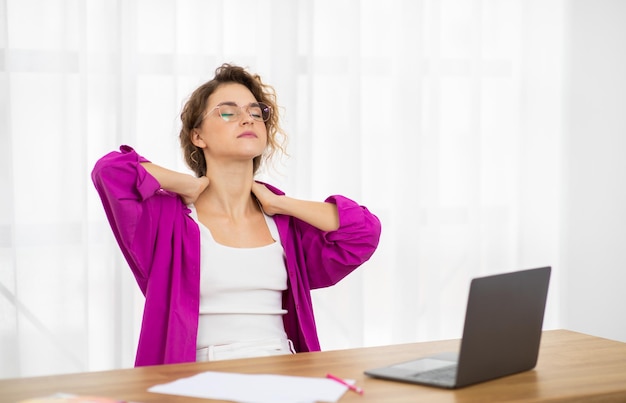 Foto mujer independiente cansada masajeando el cuello inflamado después de trabajar en una laptop en casa