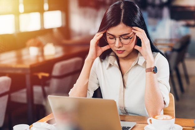 Mujer independiente de estilo de vida que trabaja en una computadora portátil, él tiene dolor de cabeza infeliz en el trabajo, usa la cabeza de mano en una cafetería