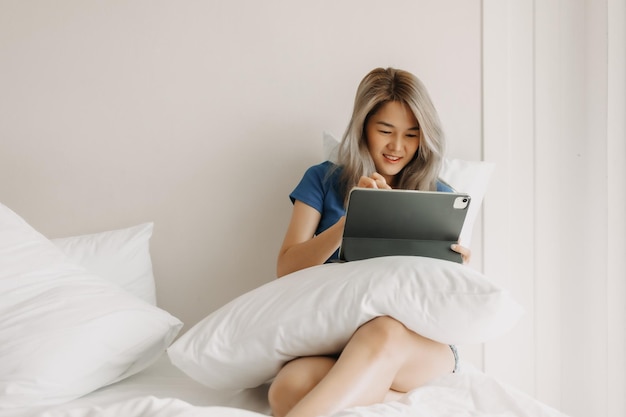 Mujer independiente feliz trabajando en la tableta en la cama del hotel en un viaje de viaje