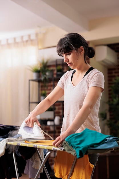 Mujer independiente que usa la plancha de vapor en casa, aprovecha para hacer las tareas del hogar los fines de semana. Esposa cuidando de las tareas del hogar antes de comenzar una semana de trabajo ocupada.