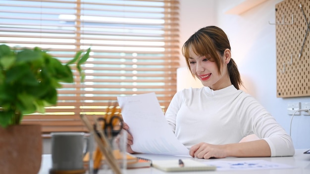 Mujer independiente sonriente está leyendo el documento de estadísticas de trabajo remoto desde casa