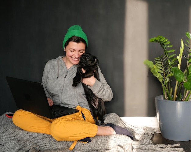 Mujer independiente trabaja con una computadora portátil en la oficina en casa con un estudio de perro mascota en línea o trabaja con una mascota en ho