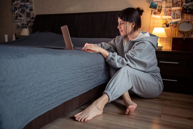 Mujer independiente trabajando en casa en una computadora portátil sentada en la computadora portátil del piso en la cama
