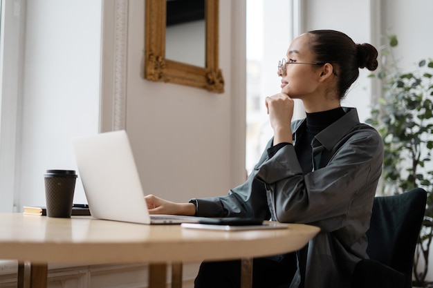 Una mujer independiente usa una computadora portátil en la oficina y escribe un mensaje a un colega